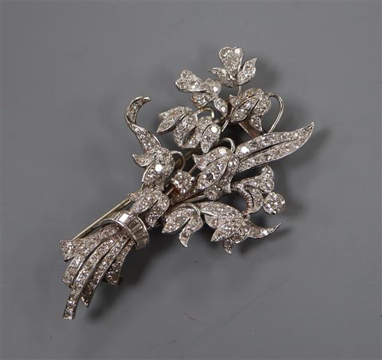 A white metal (tests as 18ct) and graduated baguette and round cut diamond set floral spray clip brooch, 57mm, gross 16.7 grams.